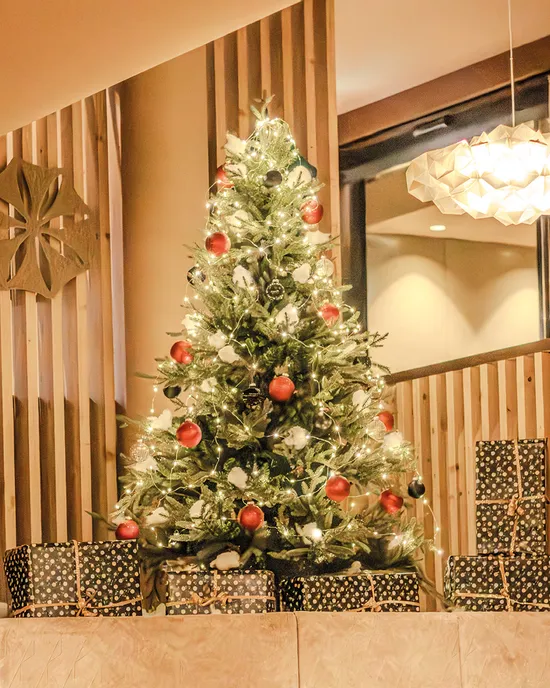 Geschmückter Weihnachtsbaum mit Lichtern und roten Kugeln von Geschenken umgeben im Innenbereich